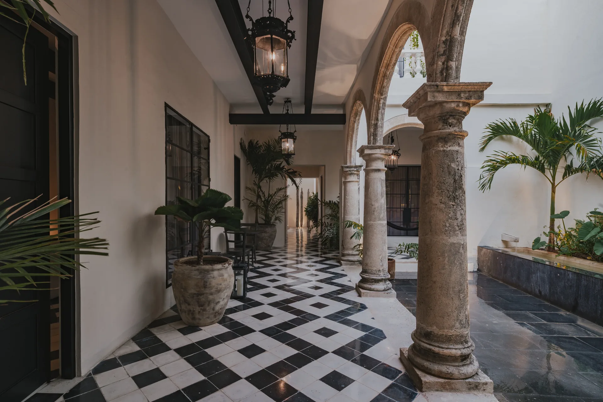 Corredor con piso de damero, palmera y arcos en una casa colonial restaurada de Campeche — Casa Japa by Casonas MX